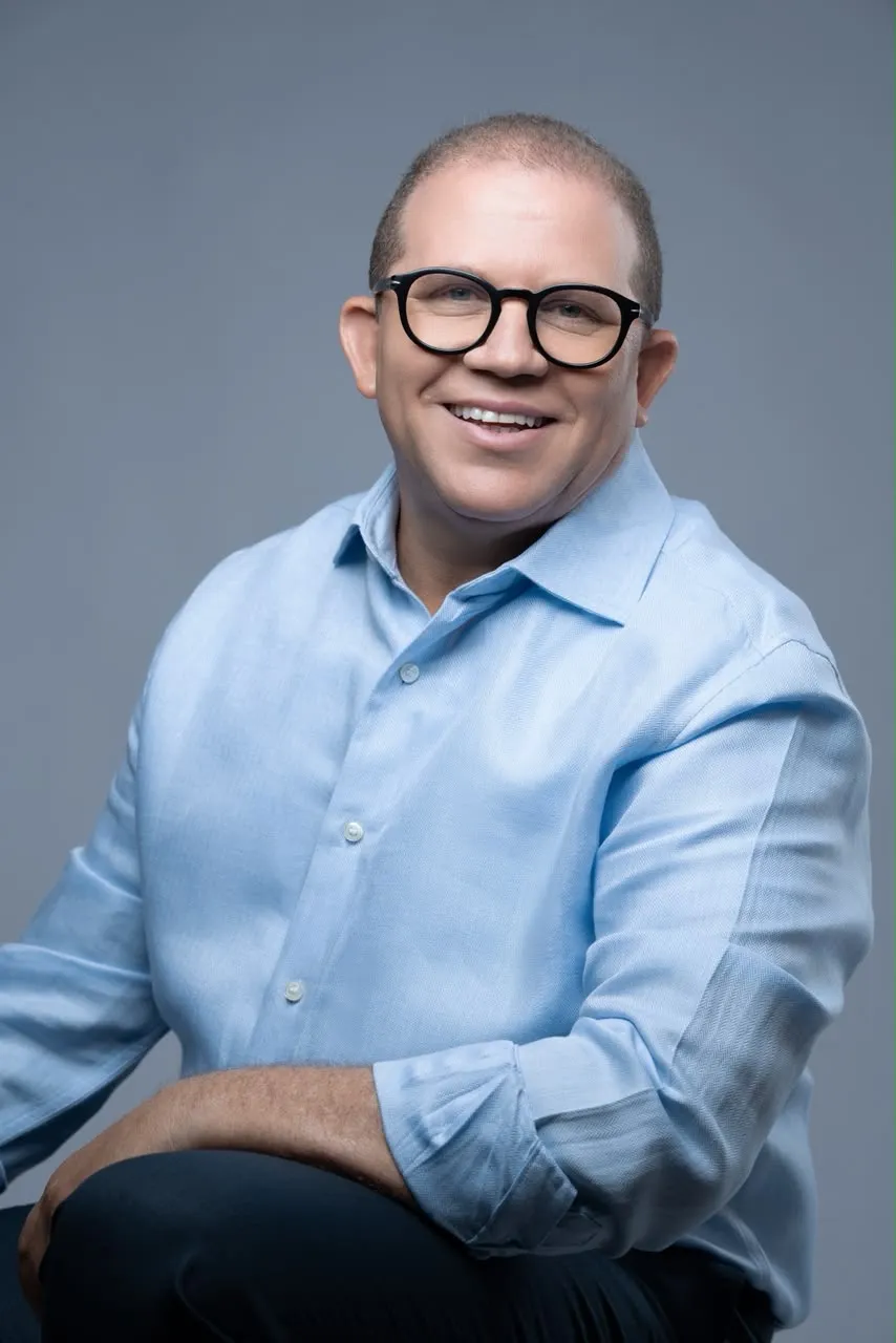 Rafael Castillo sonriendo, con camisa azul claro y lentes